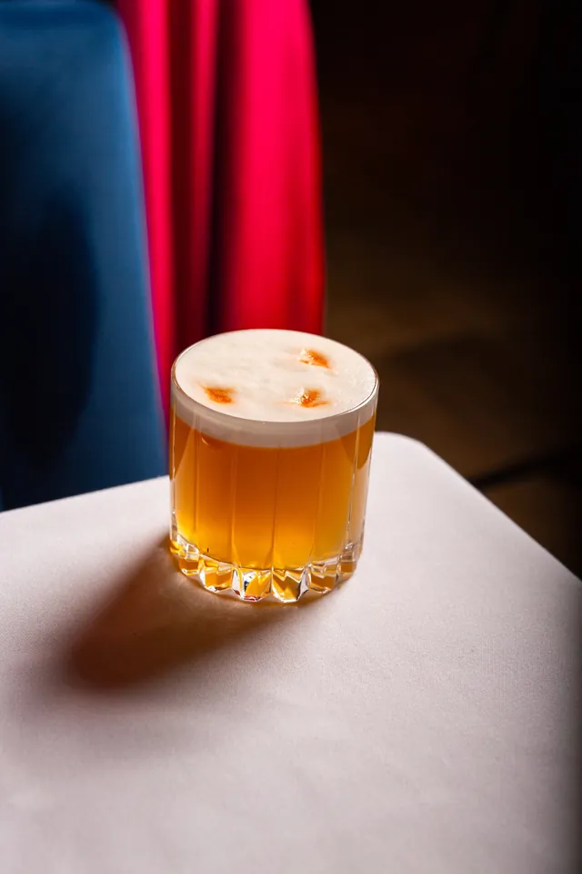 A cocktail with a foam top and orange garnish in a rocks glass at Sei Less