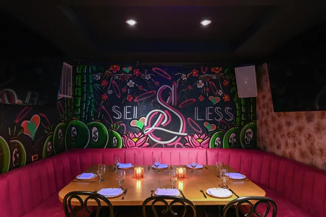 A pink booth set for dinner below the neon Sei Less sign in the Graffiti Room