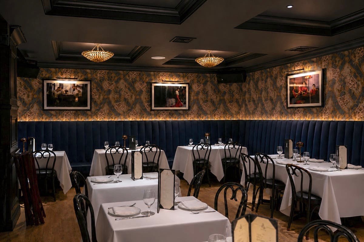The dining room at Sei Less — floral wallpaper, navy velvet banquettes and white-linen tables under gold chandeliers in Midtown Manhattan