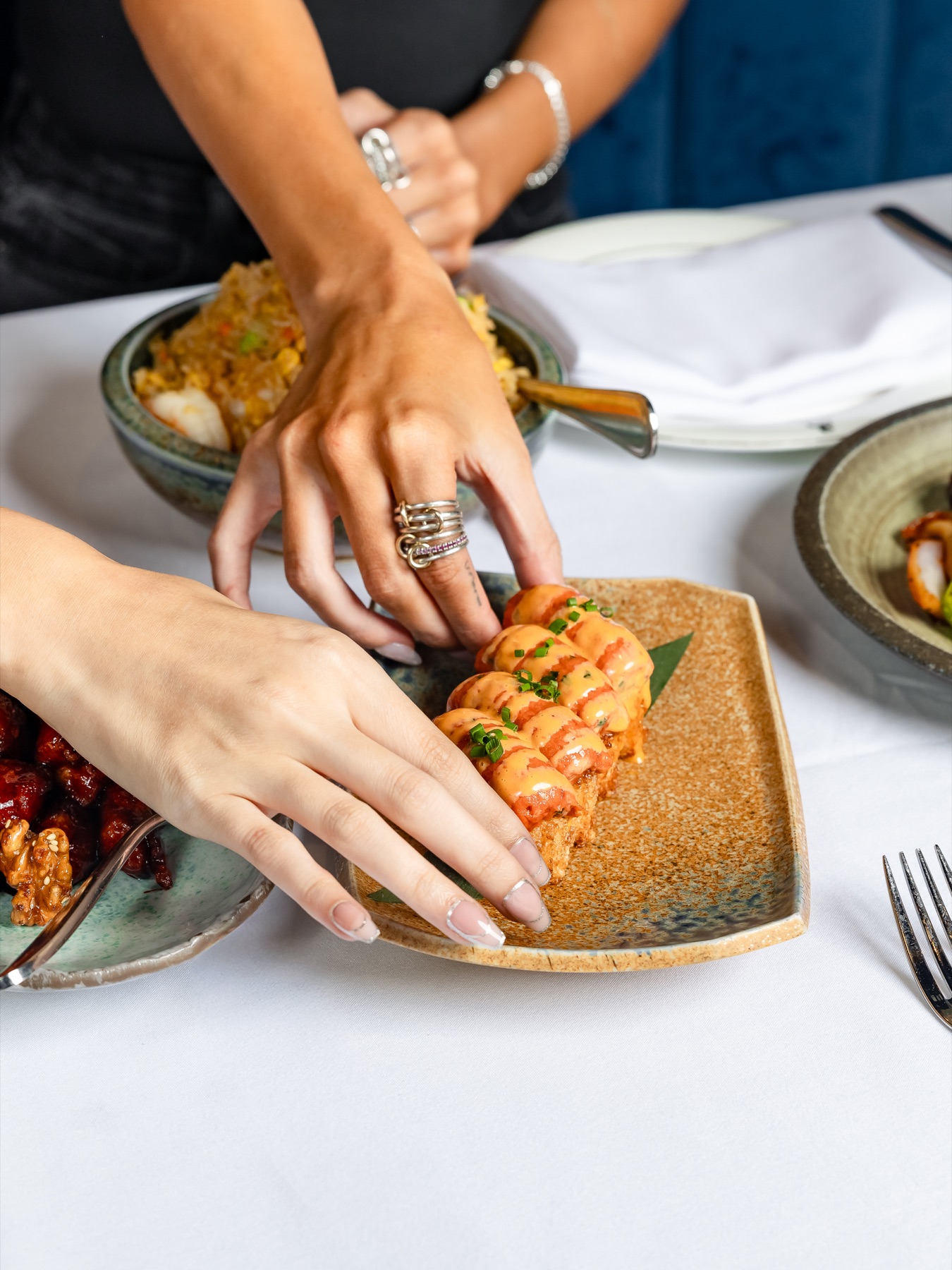 Guests sharing spicy tuna crispy rice and other Sei Less small plates on a white-linen table