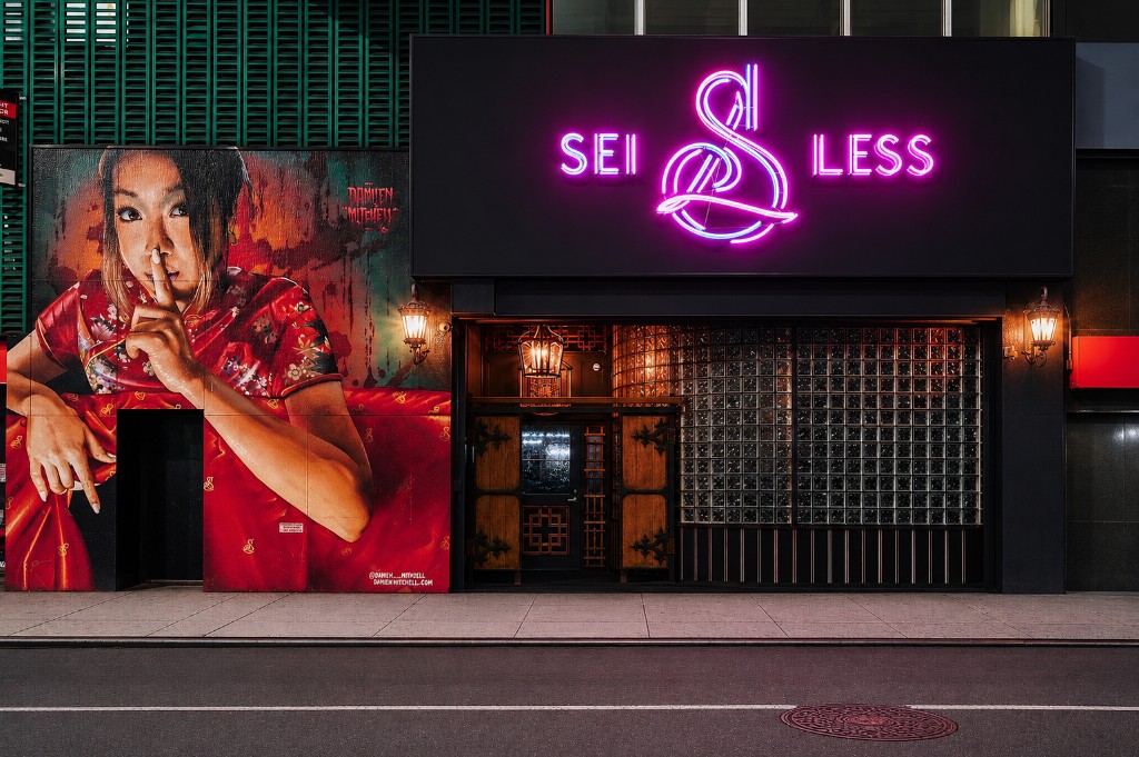Sei Less storefront at 156 West 38th Street in Midtown Manhattan — pink neon sign above the entrance and the Damien Mitchell mural